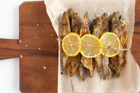 Fried capelin with lemon on baking paper on a gray background.