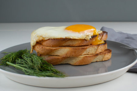 Breakfast of fried egg and croutons, dill. Gray background. Horizontal orientation. The yolk flows...