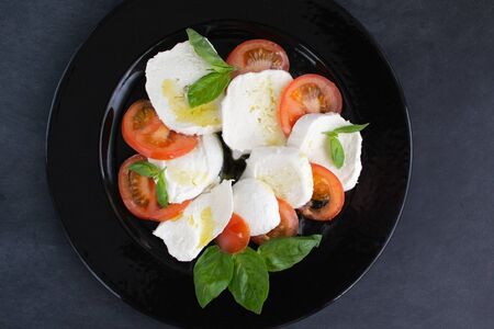 Large juicy mozzarella and small pieces of fresh tomato, a few twigs or basil leaves - if you add olive oil, you will get a delicious Caprese salad. Healthy food.の写真素材