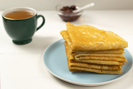 Pancakes (Russian Blini) with strawberry jam and tea on a white background. Breakfast. Ð¡lose up.