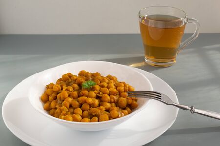 Braised chickpeas with onions and curry in a white plate on a grey background. Vegetarian food. Healthy eatingの写真素材