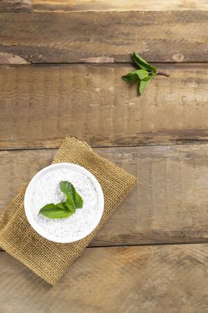 Chia pudding with mint leaves in a white bowl on a wooden background. Rustic style. Copy space. A healthy snack consists of yogurt and grains. Vertical orientation. Selective focusの写真素材