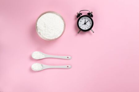 Collagen powder in a bowl with two teaspoons and a clock on a pink background. Top view. Copy space.の写真素材