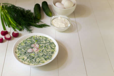 Cold soup in a deep white plate with ingredients on a white table. Okroshka, a traditional dish of Russian cuisine. Copy space.の写真素材