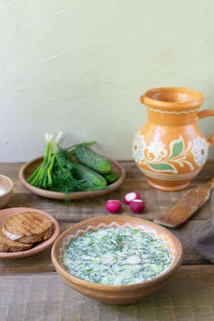 Okroshka, a traditional dish of Russian cuisine. Cold soup in a deep plate with a jug on a wooden table. Rustic style.の写真素材