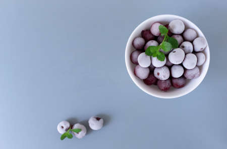 Frozen cherries with sprigs of mint in a white bowl on a gray background. Copy space. Top view.の写真素材