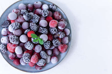 Frozen berries in a gray plate with a sprig of mlisa on a white background. Copy space. Top view. Close-upの写真素材