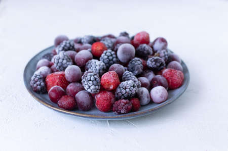 Frozen berries in a gray plate on a white background. Copy space. Close-up. Selective focus.の写真素材