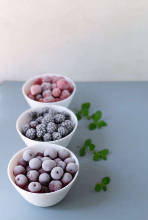 Frozen berries in a white bowls on a gray background .. Copy space. Close-up. Selective focus. Vertical orientation.の写真素材