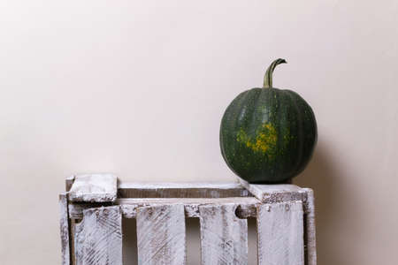 A round dark green pumpkin stands on a white wooden box on a yellow background. Copy space. Horizontal orientation.の写真素材