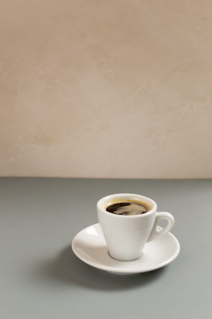 White cup with espresso coffee on a white saucer on a gray background. Selective focus. Copy space....