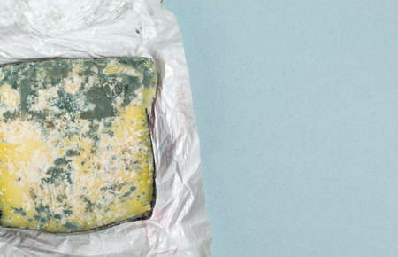 Spoiled cheese in a white package on a blue background. Food waste concept. Top view. Horizontal orientation. Copy space.の写真素材