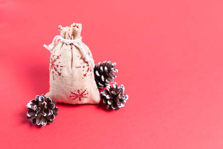 Natural bag with gifts and pine cones on a red background. Natural Christmas decor concept. Copy space.の写真素材