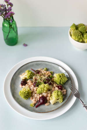 Natural salad of mini beets, romanesco cabbage, white beans and sprouted onion seeds on a gray plate. Healthy nutrition concept. Selective focus. Copy space. Vertical orientation.の写真素材