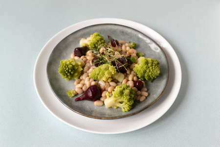 Natural salad of mini beets, romanesco cabbage, white beans and sprouted onion seeds on a gray plate. Healthy nutrition concept. Selective focus. Copy space.の写真素材