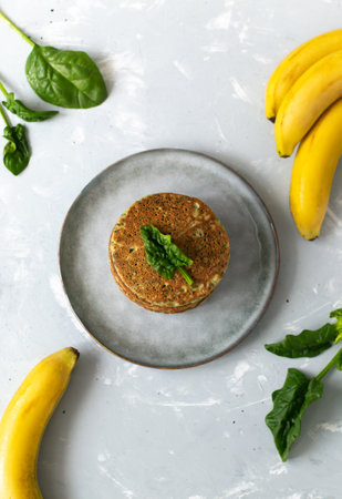 Spinach and banana pancakes and green leaves and bright fruits on a gray plate on a gray background. Healthy food concept. Copy space. Vertical orientation. Top view.の写真素材