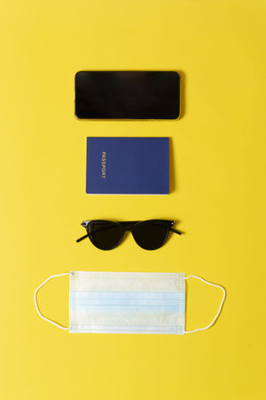 Summer hat, passport, sunglasses and a medical protective mask lie on a yellow background. Travel...
