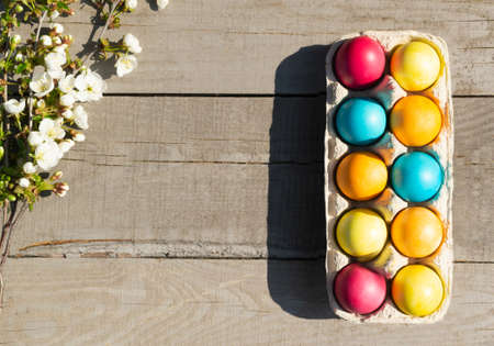 Easter colorful eggs with a branch of a blossoming apple tree on a wooden background. Christian holiday concept. Horizontal orientation. Copy space.の写真素材