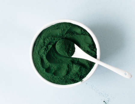 Chlorella powder in a white bowl with a teaspoon on a blue background. Superfood concept. Horizontal orientation. Top view.の写真素材