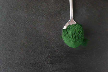 Chlorella powder in a metal spoon on a stone background. Healthy food concept. Horizontal orientation. Top view. Copy space.の写真素材