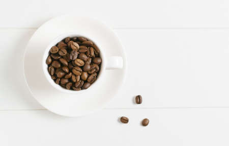 Coffee beans in a white espresso cup with several grains on a white background. Coffee concept. Top view. Copy space.の写真素材