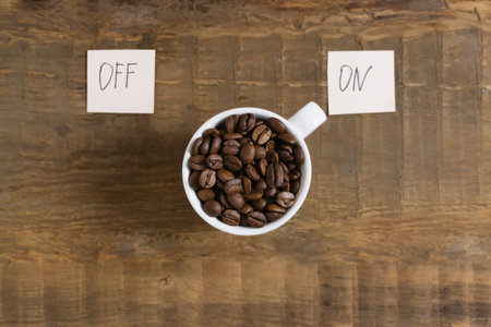 Coffee beans in a white cup with the words on and off on pieces of paper on a wooden background. Top view. Morning coffee concept.の写真素材
