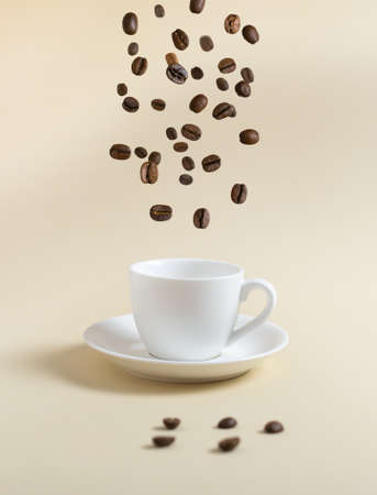 Coffee beans are flying into a white espresso cup on a yellow background. Flying food concept.の写真素材