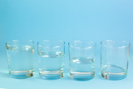 Four glass glasses with water stand on a blue background. Waste water concept. Horizontal orientation.の写真素材