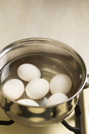 White chicken eggs are boiled in a ladle with wate on the stove in the home kitchen. Healthy food concept. Vertical orientation.の写真素材