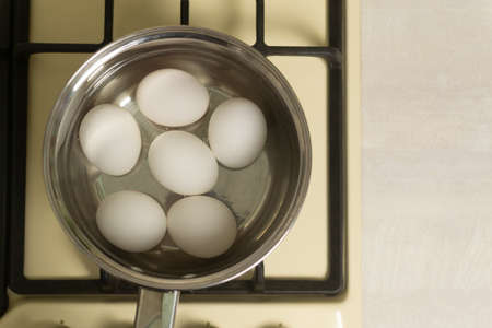White chicken eggs are boiled in a ladle with wate on the stove in the home kitchen. Healthy food concept. Horisontal orientation. Top view.の写真素材
