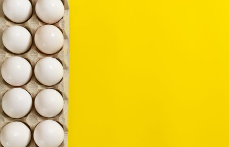White chicken eggs lie in an egg tray on yellow background. Healthy food concept. Horisontal...