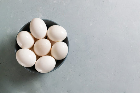 White chicken eggs lie in a gray bowl on a gray background. Diet food concept. Copy space. Top view.