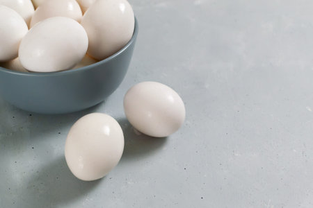 White chicken eggs lie in a gray bowl on a gray background. Diet food concept. Copy space.