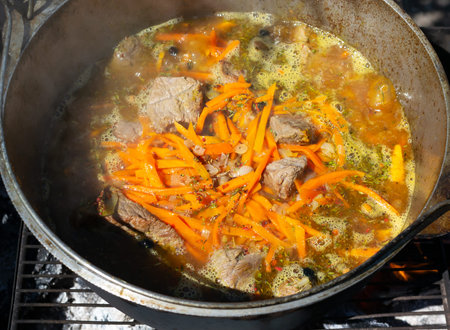 Cooking traditional oriental pilaf in a cauldron over a fire. Stewed pieces of meat and onions,...
