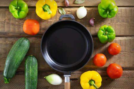 Cast iron frying pan among multi-colored vegetables on a wooden background. Top view. Traditional Spanish cuisine concept.の写真素材