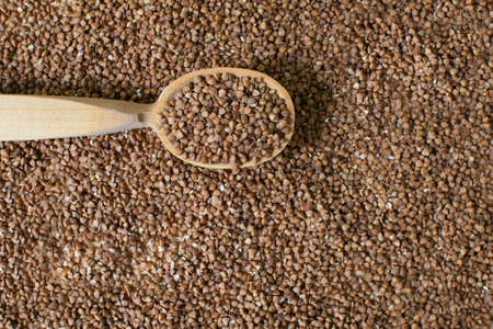 A wooden tablespoon lies on dry buckwheat, raw grains. Texture. Healthy nutrition concept. Horizontal orientation. Buckwheat contains a large amount of vitamins and minerals. Top view.の写真素材