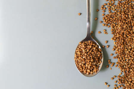 A metal tablespoon with dry buckwheat is on a gray background. Healthy nutrition concept. Horizontal orientation. Buckwheat contains a large amount of vitamins and minerals. Top view. Copy space.の写真素材