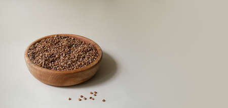 Organic buckwheat groats in a wooden bowl on a light background. Minimalism. Rustic style. Healthy nutrition concept. Horizontal orientation. Copy space. Banner.の写真素材