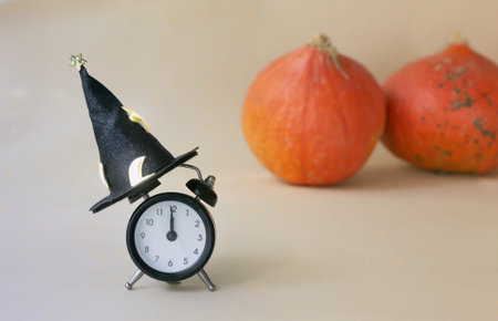 A clock in a magic hat with pumpkins in the background on a light background. The concept of...