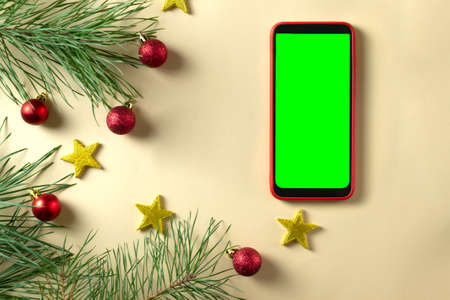 Happy New Year 2022 greeting card. Smartphone and several pine branches with red balls and gold stars. Celebration atmosphere. Top view. Green screen.の写真素材
