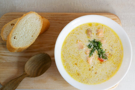 Salmon and cream fish soup in a white bowl on a wooden cutting board with a few slices of bread....