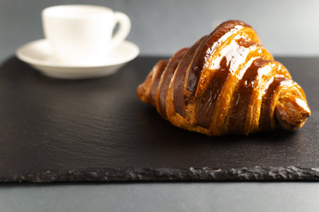Freshly backed french croissant with chocolate filling lies on the slate board with a cup of hot drink. Beautiful and delicious pastries. Copy space. Selective focus.の写真素材