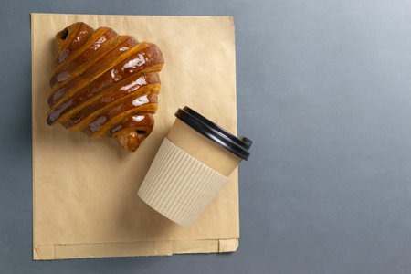 French croissant on a craft bag with a paper cup in the background. Takeaway food concept. Beautiful and delicious pastries. Copy space. Horisontal orientation. Top view.の写真素材