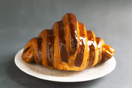 Freshly backed french croissant with chocolate filling lies on a white saucer on a gray table. Traditional bakery concept.の写真素材