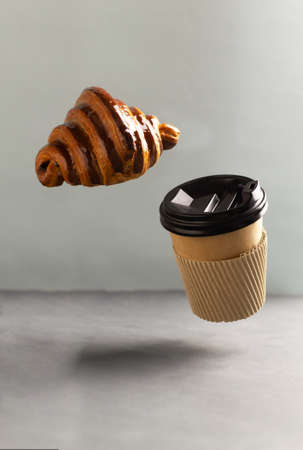 French croissant and paper cup on gray background. Flying food. Takeaway food concept. Beautiful and delicious pastries. Copy space.の写真素材