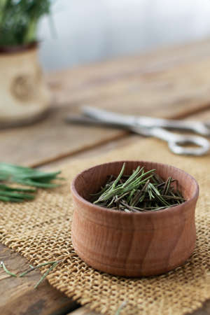 Dry rosemary in a wooden bowl with scissors on a wooden table. Rustic style. The dry spice is added to various dishes or drinks. Concept Ultra urban farming. Indoor Gardering.の写真素材