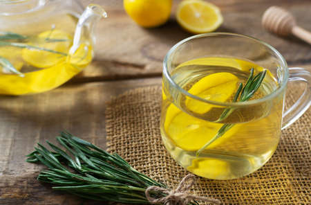 A cup of hot warming tea with rosemary, lemon and honey with ingredients and a teapot on a wooden table. Rustic style. Alternative medicine concept. Horizontal orientation. Selective focus.の写真素材
