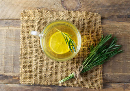 A cup of hot warming tea with rosemary, lemon and honey with a sprig of fresh sprig on a wooden table. Rustic style. Alternative medicine concept. Horizontal orientation. Top view.の写真素材