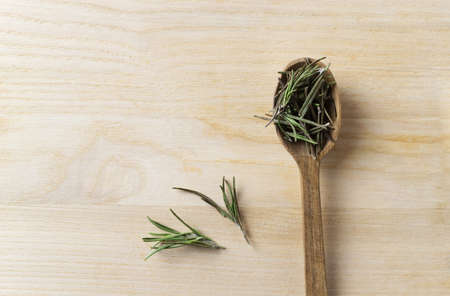 A spoonful of dried rosemary lies on a wooden table. Rustic style. The dry spice is added to various dishes or drinks. It is an ingredient for various spice mixes. Top view. Copy space.の写真素材