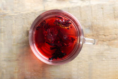 A glass cup with red hibiscus tea stands on a wooden table. The drink has a bright red color thanks to the flowers of the Sudanese rose. Traditional drinks concept. Top view. Horizontal orientation.の写真素材